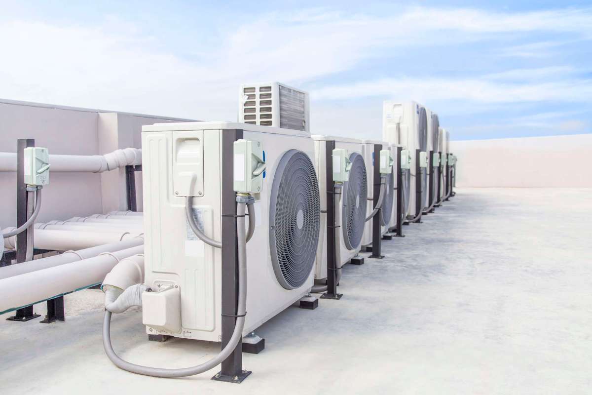 Several air conditioning units lined up on a rooftop with visible piping and clear blue skies.