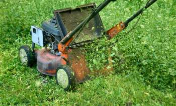A lawn mower cutting grass with clippings flying from the discharge area.