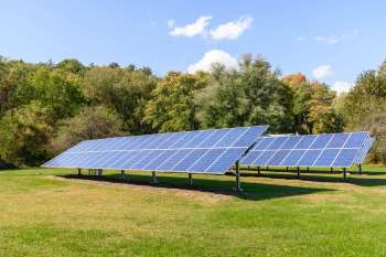 Solar panels installed on a grassy field with trees in the background.