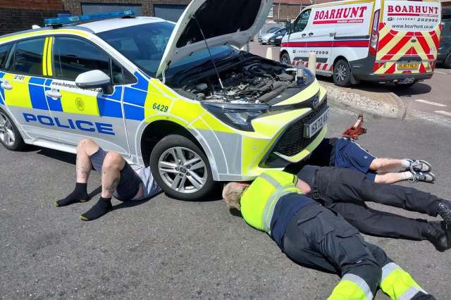 Four people looking under a car.