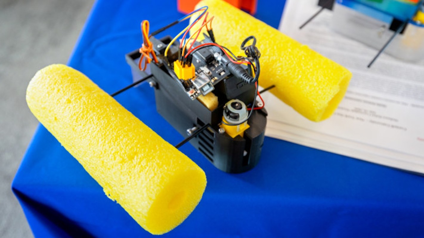 A robotic device with yellow foam floats and electronic components on a blue table.