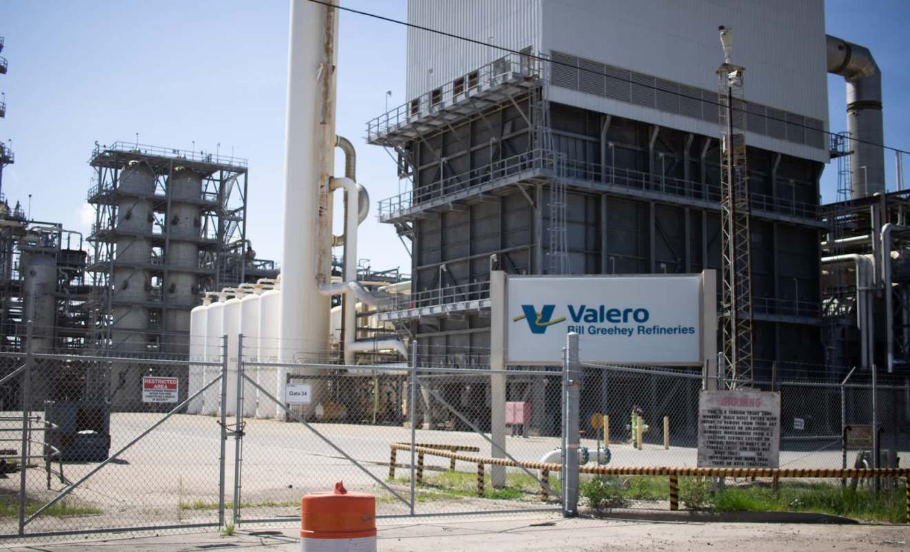 A Valero refinery with large storage tanks and industrial structures behind a fenced area.