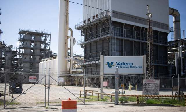 A Valero refinery with large storage tanks and industrial structures behind a fenced area.