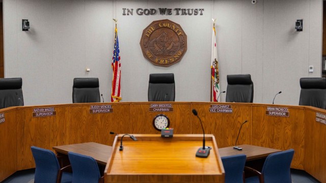 A empty government meeting room with a wooden table, chairs, and a seal on the wall.