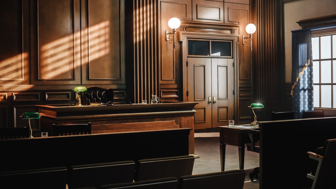 A courtroom interior featuring wooden paneling, a judge's desk, and a green desk lamp.