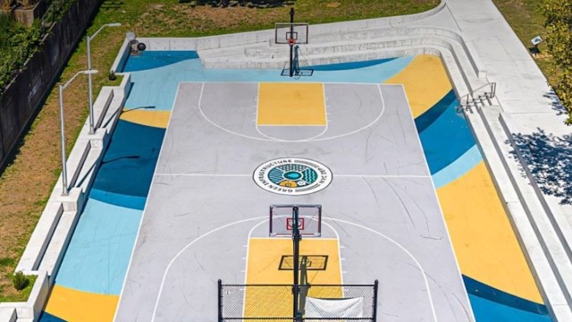 A basketball court with colorful markings and two hoops surrounded by concrete and grass.