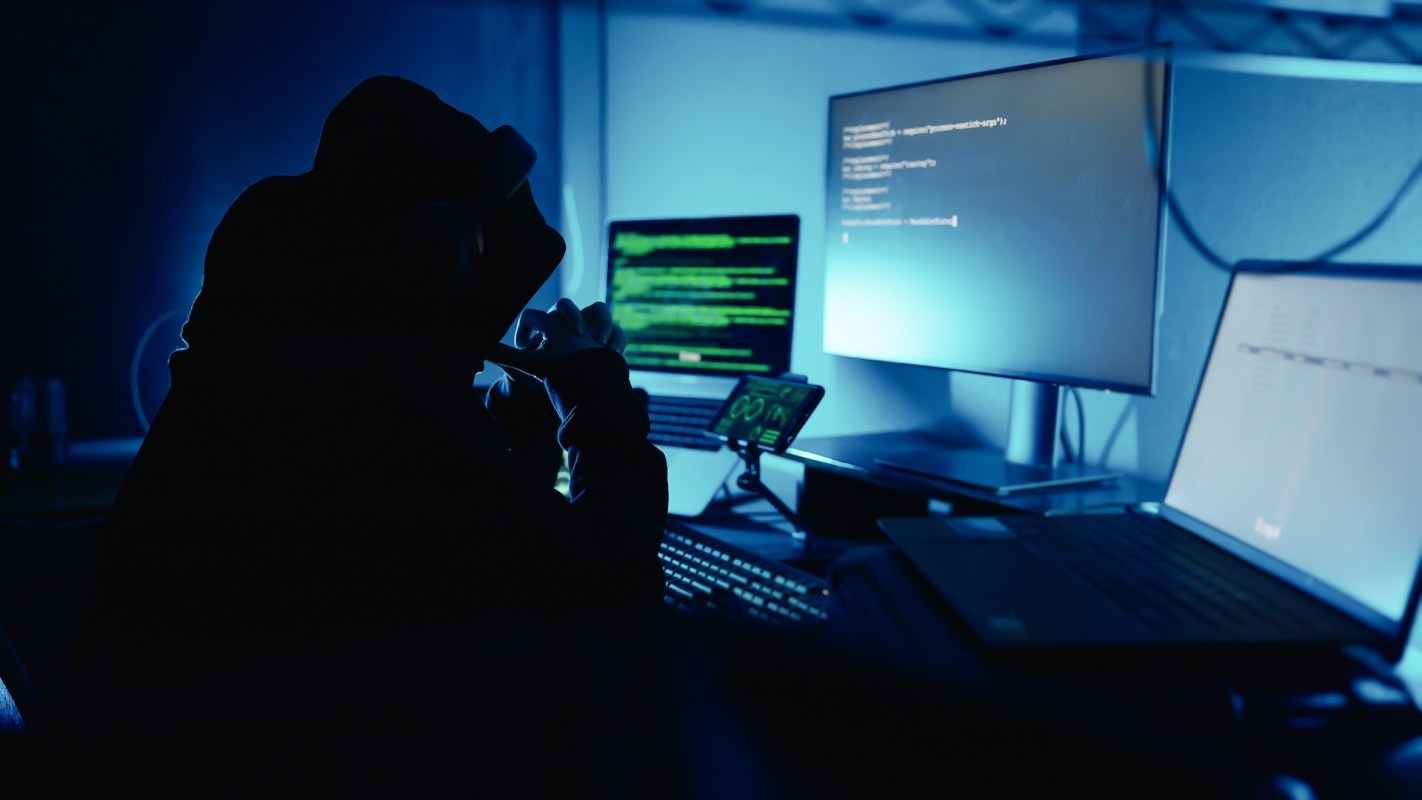 A person sitting in front of computer monitors in a dark room.