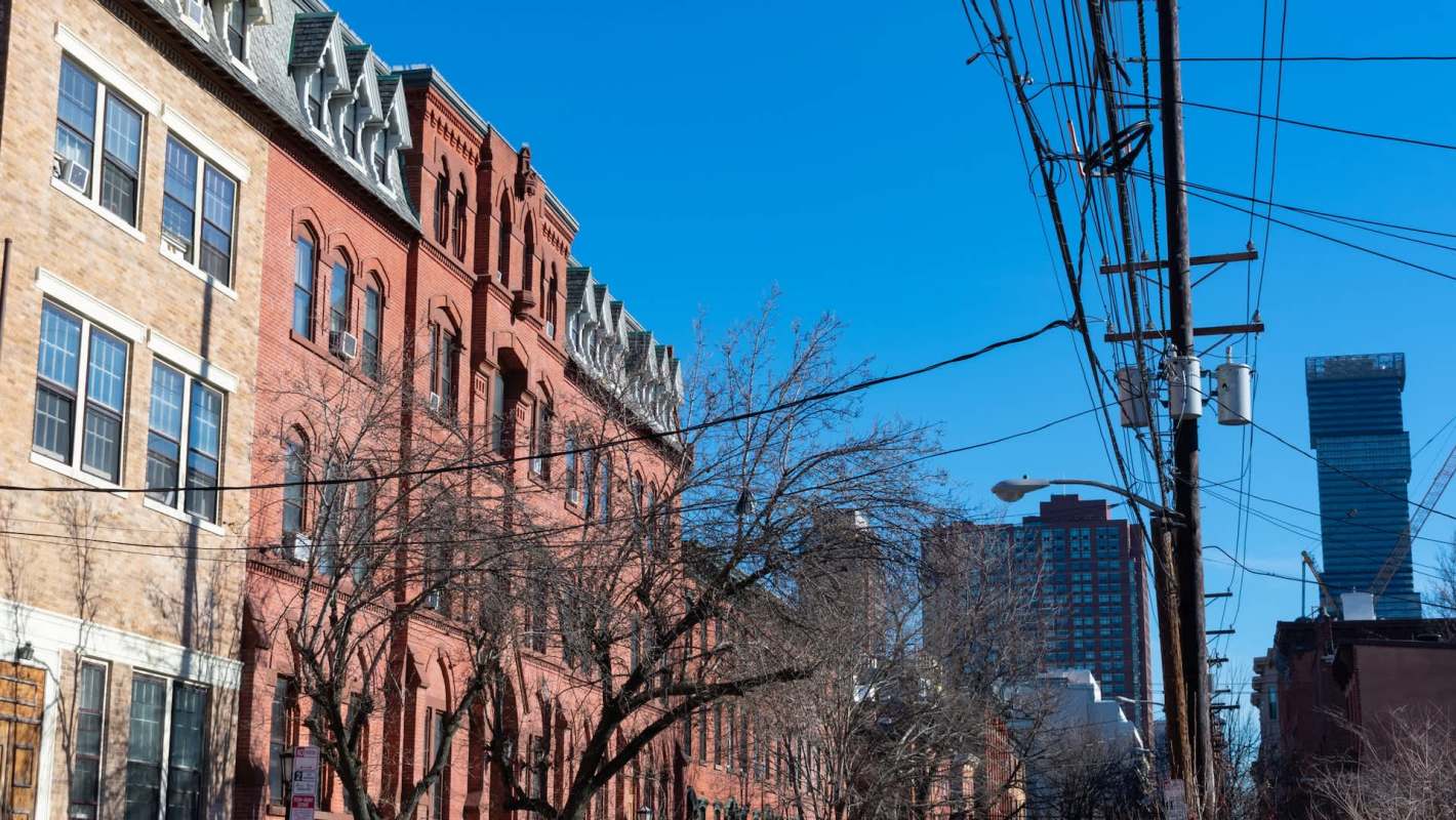 Historic brick buildings with trees and power lines under a clear blue sky, alongside modern city structures.