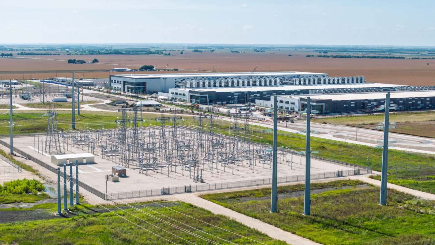 An industrial area featuring a power substation and a large data center in a rural landscape.
