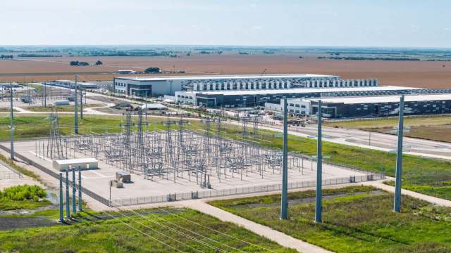 An industrial area featuring a power substation and a large data center in a rural landscape.