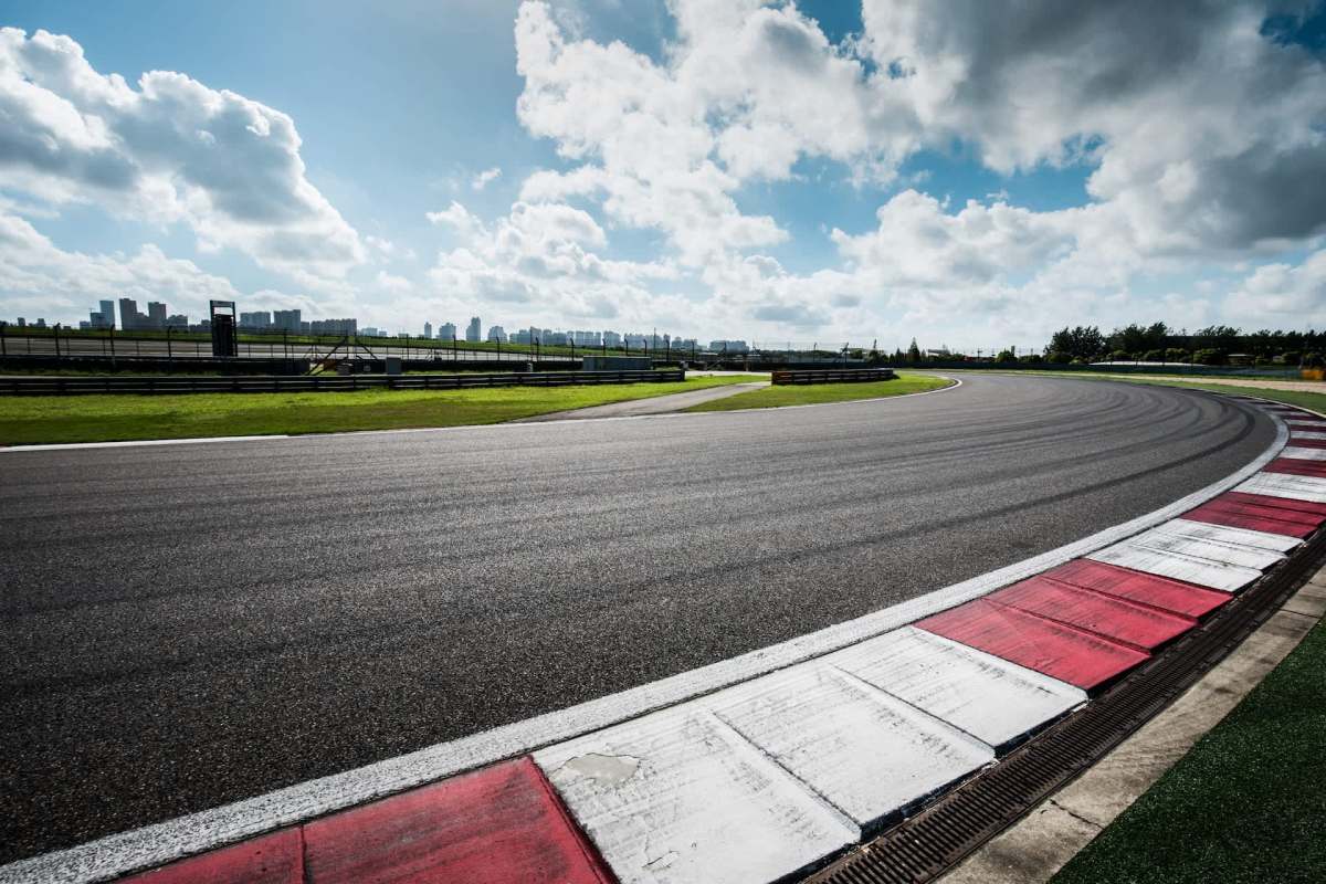 A winding race track bordered by green grass and a skyline under a partly cloudy sky.