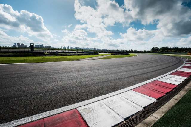 A winding race track bordered by green grass and a skyline under a partly cloudy sky.