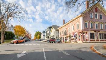 A street lined with colorful houses and parked cars under a partly cloudy sky in a small town.