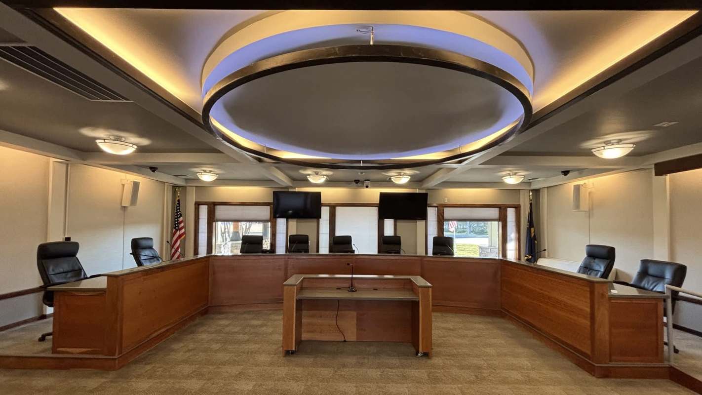 A conference room with a central table, multiple chairs, and two wall-mounted televisions.