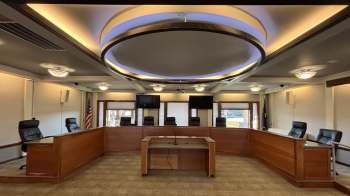 A conference room with a central table, multiple chairs, and two wall-mounted televisions.