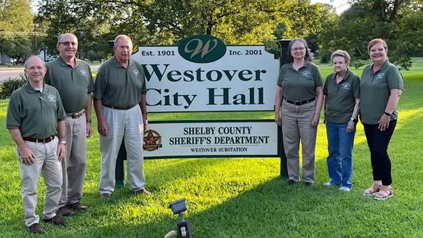A group of people in green shirts poses in front of a Westover City Hall sign.