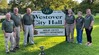 A group of people in green shirts poses in front of a Westover City Hall sign.