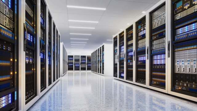 A data center with multiple server racks and bright blue lighting.