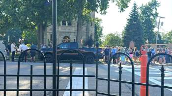 A crowd gathers in front of a town hall during an outdoor event.