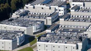 An aerial view of industrial buildings with rooftops featuring solar panels and ventilation equipment.