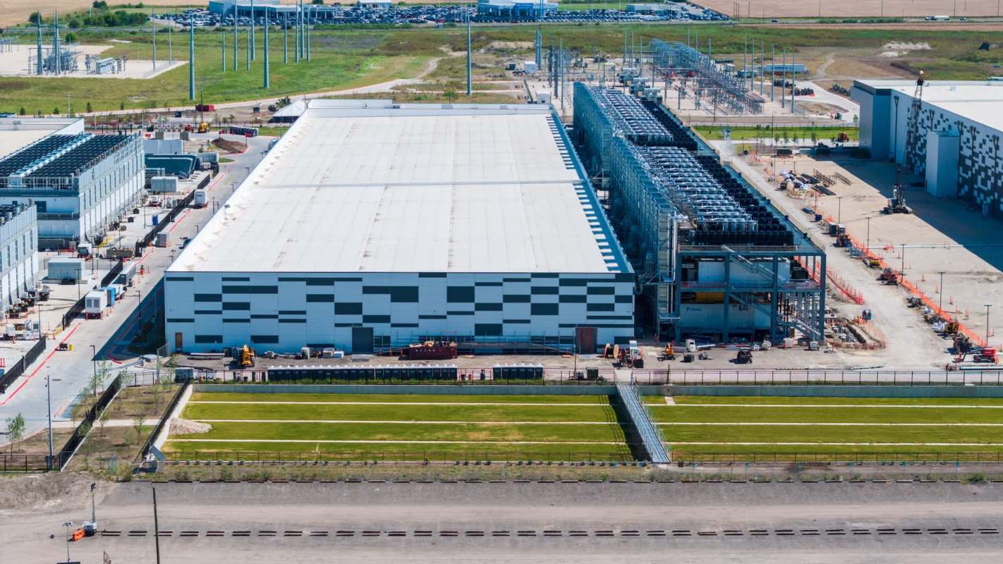 Aerial view of a large industrial facility with several buildings, parking, and construction equipment.