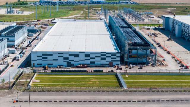 Aerial view of a large industrial facility with several buildings, parking, and construction equipment.