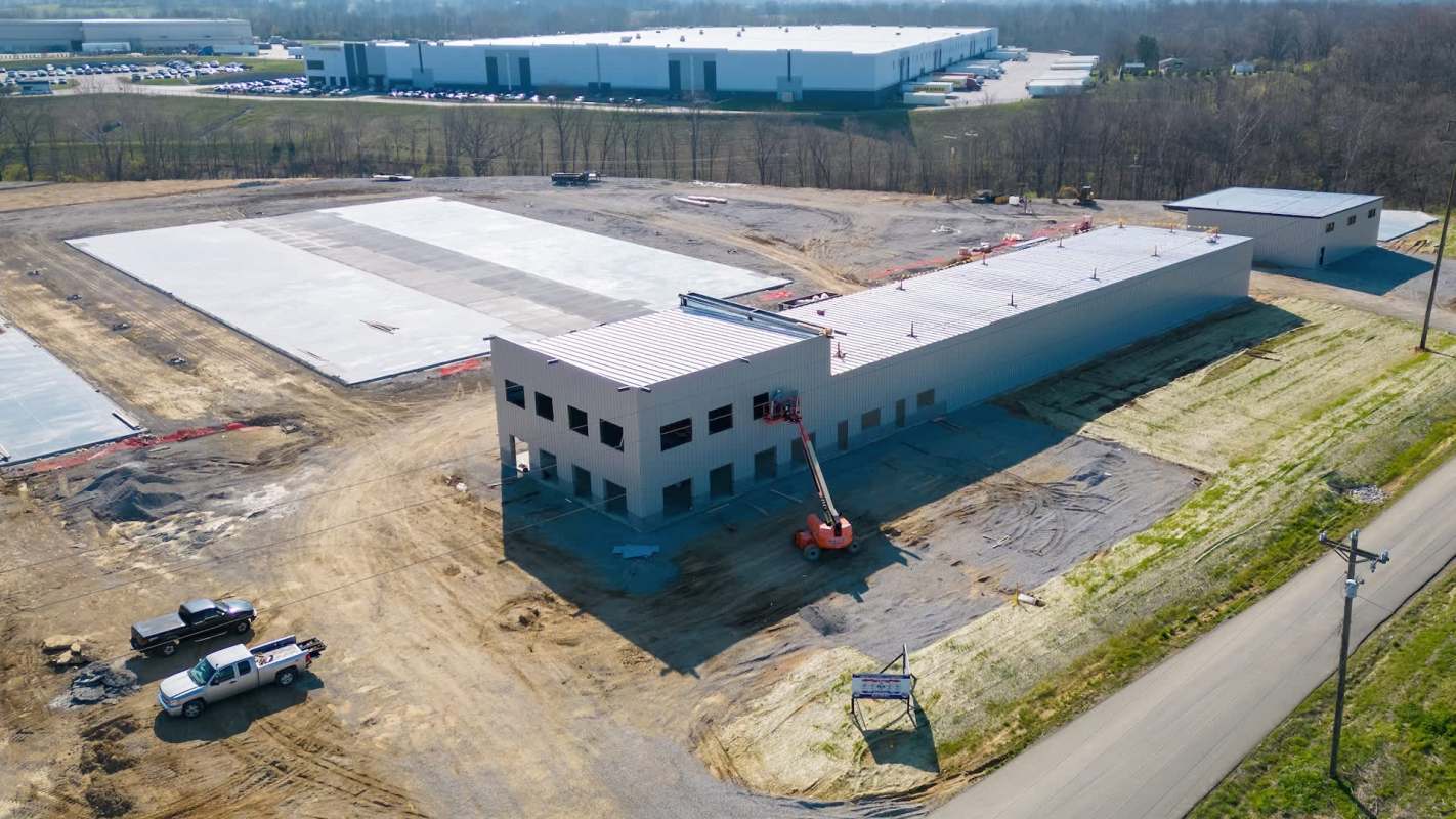 A construction site featuring a partially built warehouse and machinery on a gravel surface.