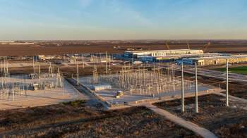 An industrial power station with electrical infrastructure and buildings under a clear sky.