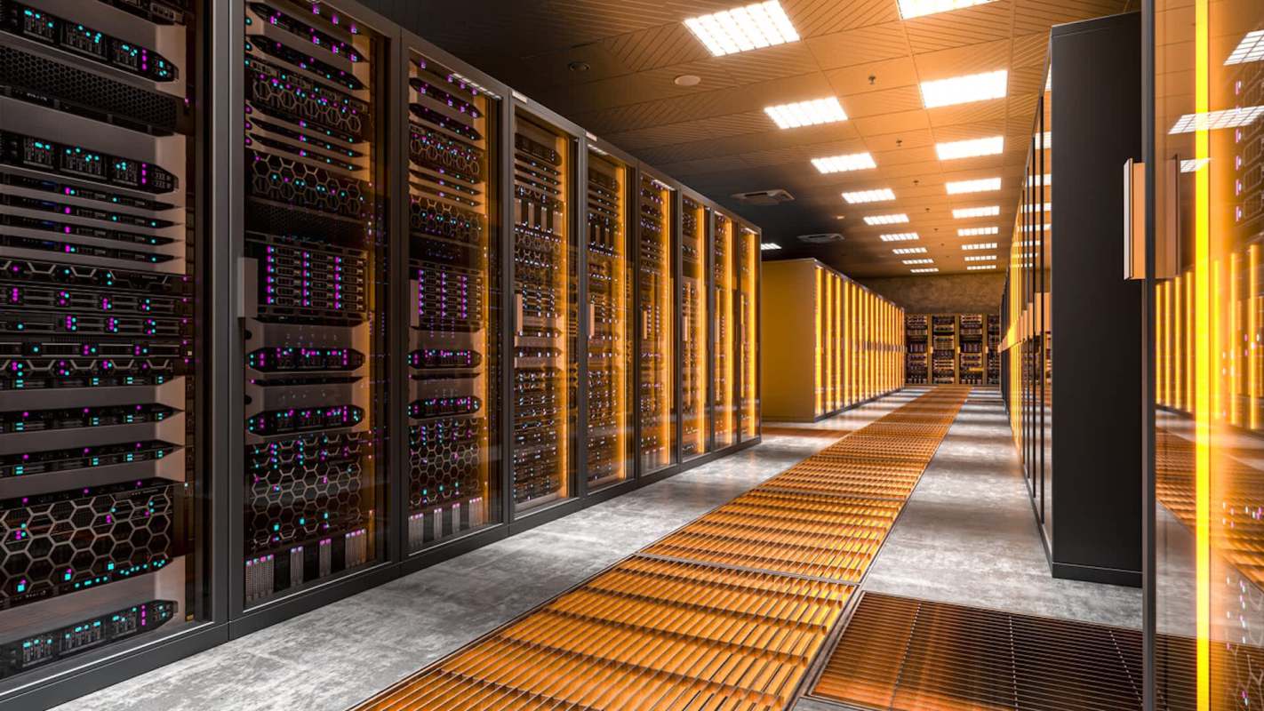 A data center aisle lined with server racks and illuminated with orange lighting.