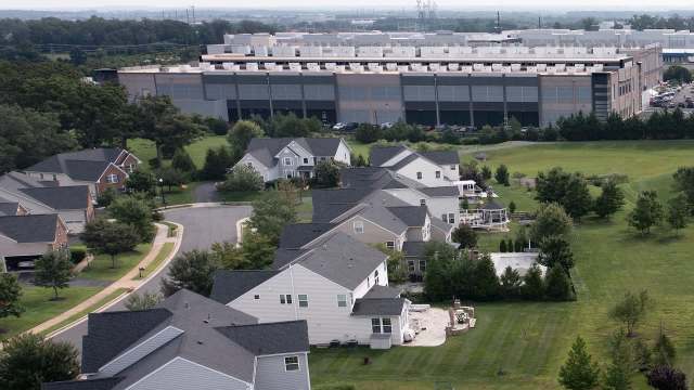A residential neighborhood with houses, lawns, and a large industrial building in the background.