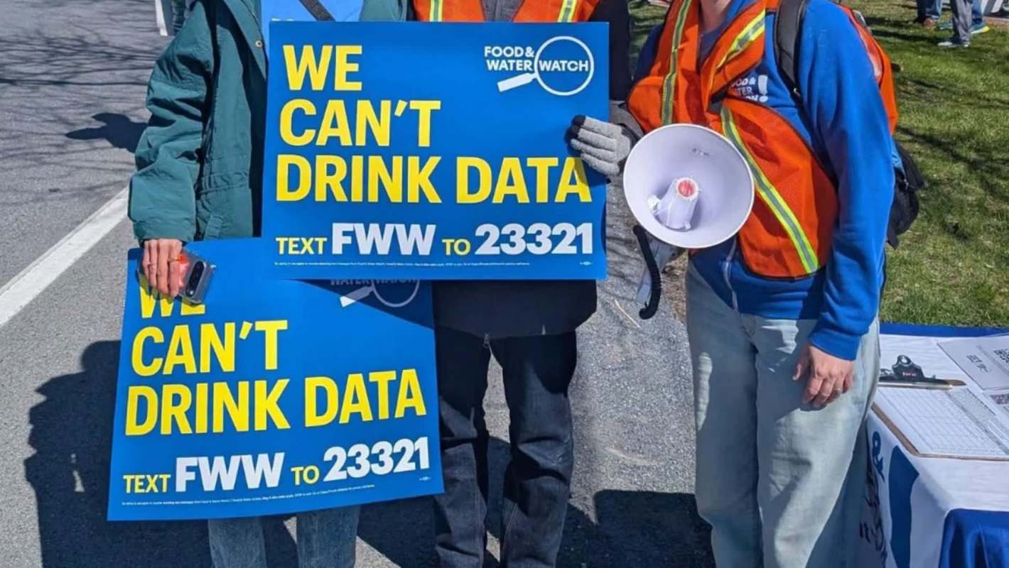Three people hold protest signs that read "WE CAN'T DRINK DATA" while one holds a megaphone.