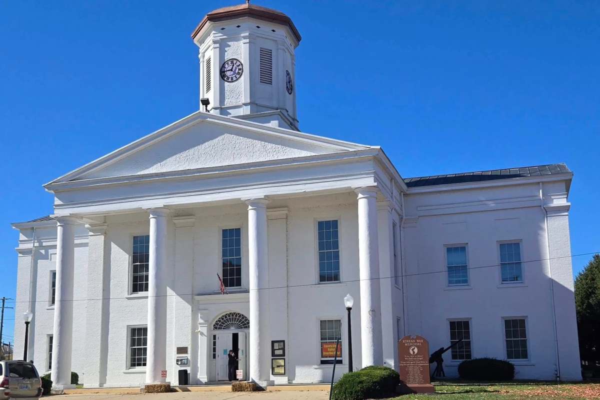 A white historical building with columns, a clock tower, and a sign honoring veterans.