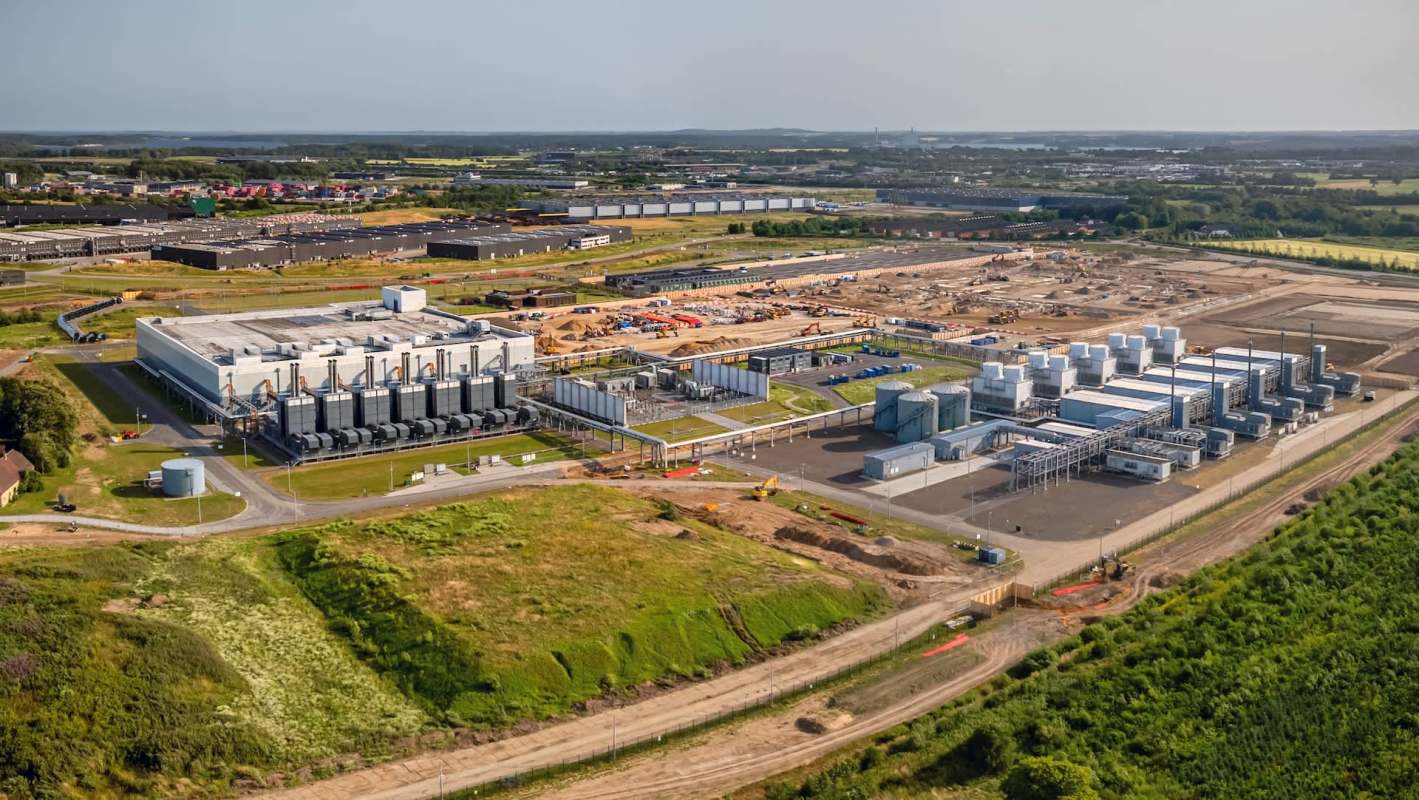 An industrial facility with multiple buildings and equipment, surrounded by construction sites and green land.