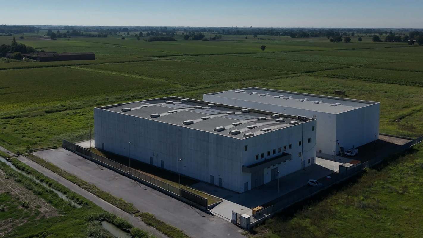 A large industrial building surrounded by green fields and open land.