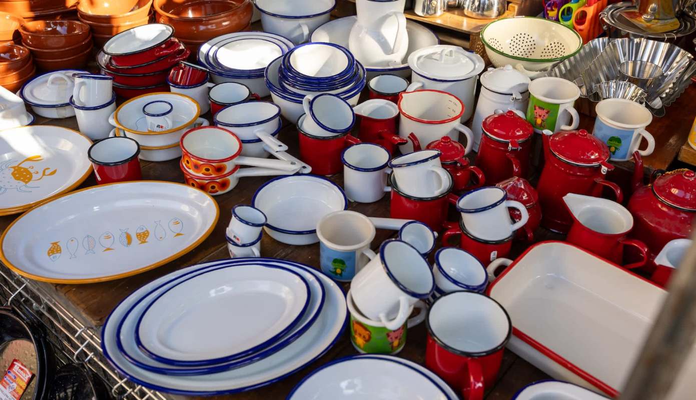 A collection of various ceramic and enamel dishware in red, white, and blue, displayed on a wooden surface.