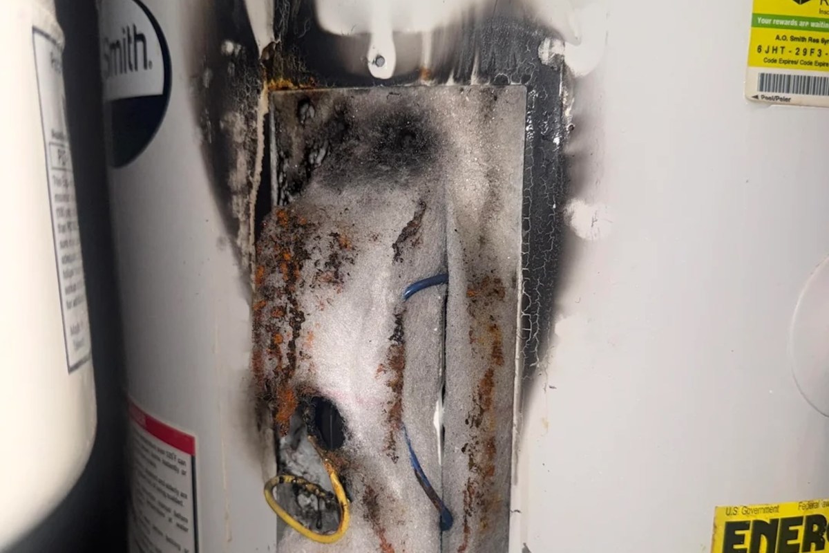A water heater with visible burn marks, rust, and damaged insulation around electrical components.