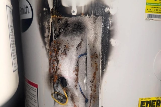 A water heater with visible burn marks, rust, and damaged insulation around electrical components.