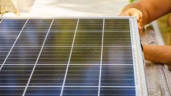 A person is handling a solar panel on a work surface.