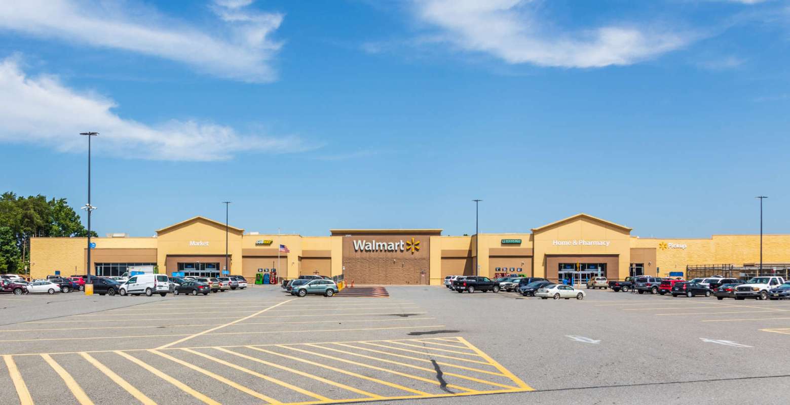 A Walmart store with various entrances and a large parking lot on a clear day.