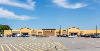 A Walmart store with various entrances and a large parking lot on a clear day.