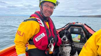 A lifeguard in a boat with a rescue dog and navigational equipment on a calm sea.