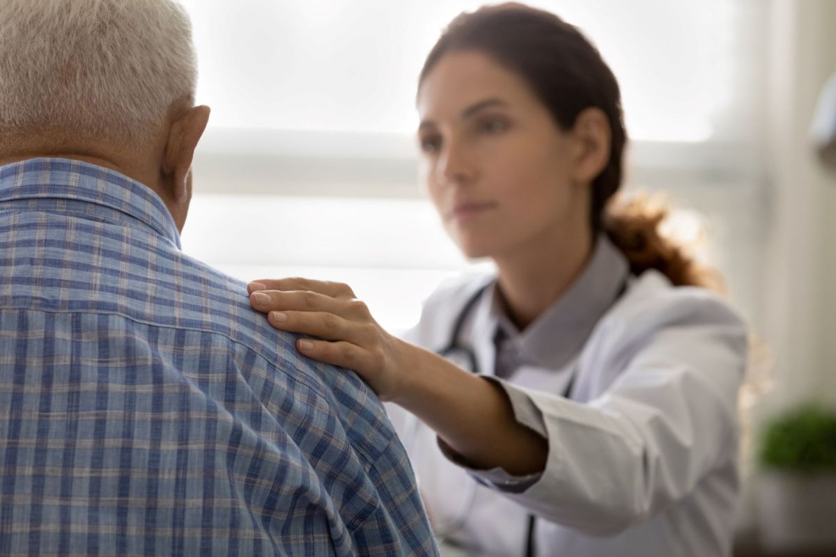 A healthcare professional touches the shoulder of an elderly patient in an office setting.
