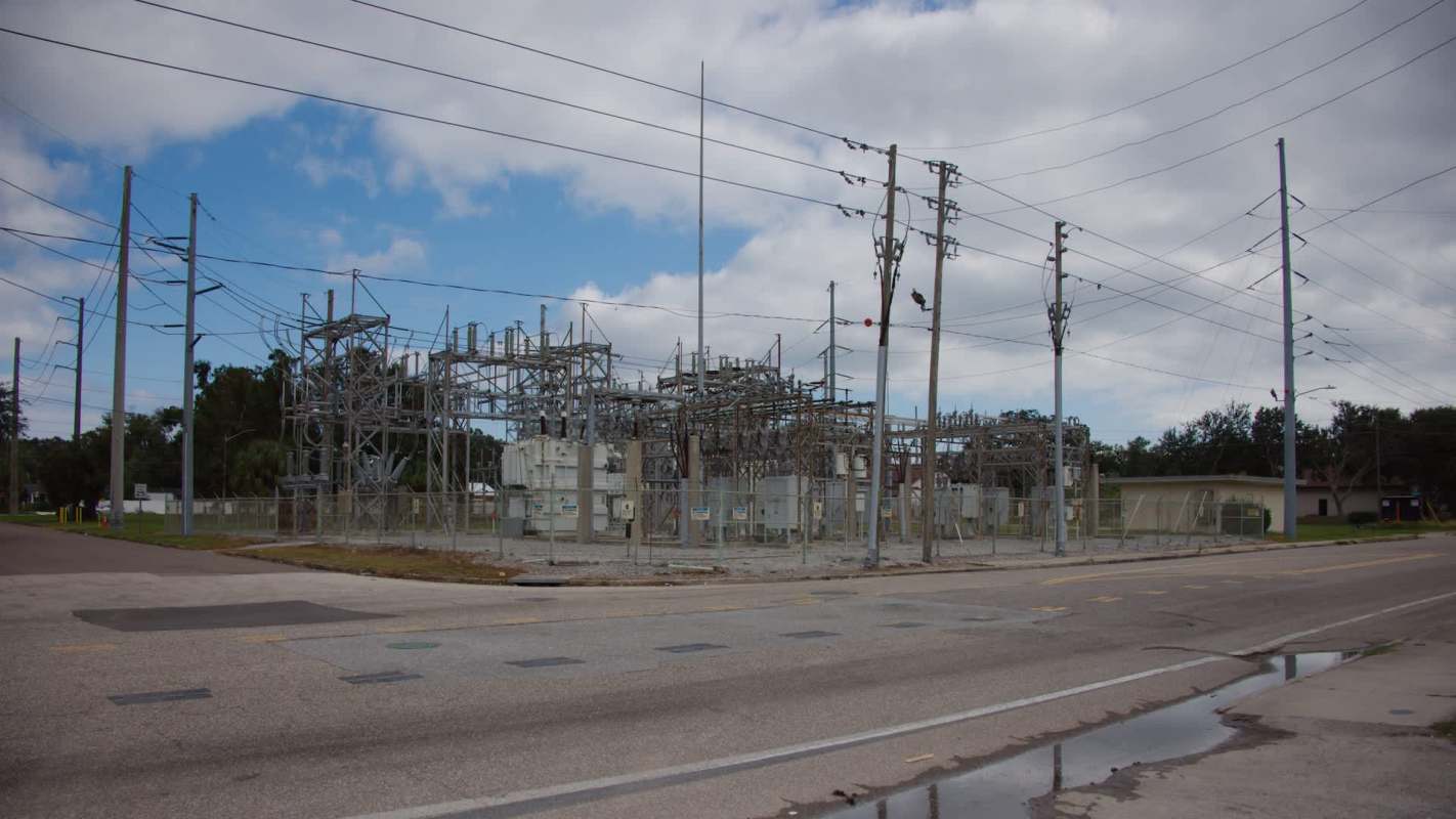An electrical substation with towers, power lines, and a fenced area next to a road.