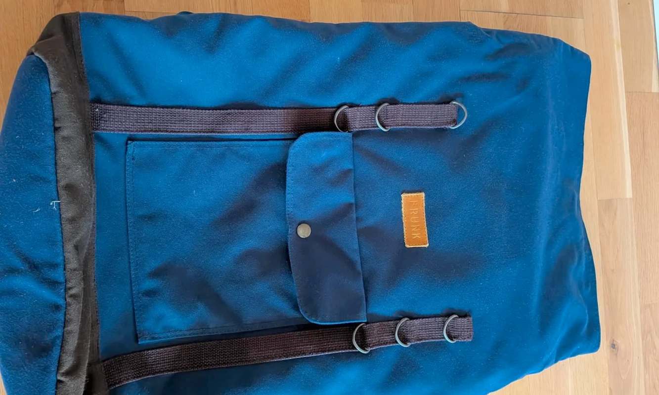 A blue backpack with a front pocket and straps laid on a wooden surface.