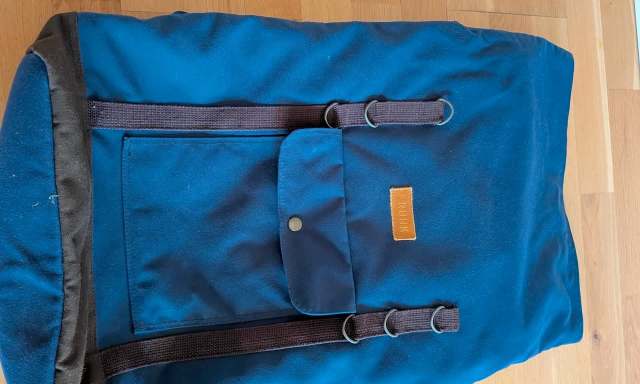 A blue backpack with a front pocket and straps laid on a wooden surface.