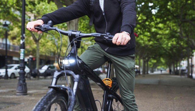 A person rides a black bicycle along a tree-lined street.