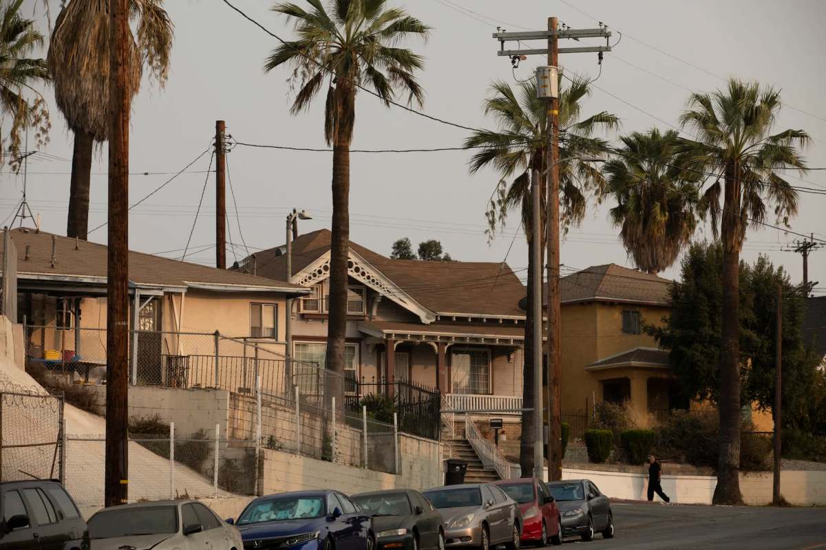 A street view of East Los Angeles, featuring palm trees, houses, and parked cars.