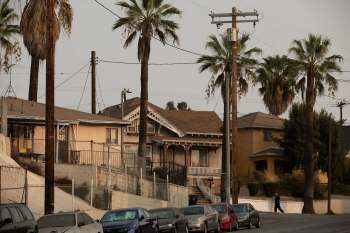 A street view of East Los Angeles, featuring palm trees, houses, and parked cars.