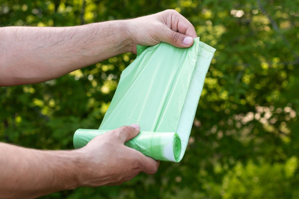A man holding a roll of green garbage bags.