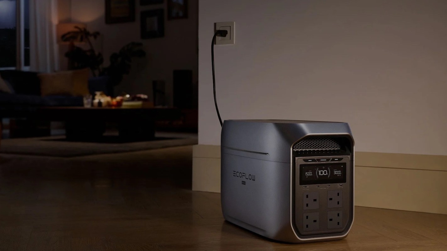A portable power station with multiple outlets, plugged in against a wall in a dimly lit room.